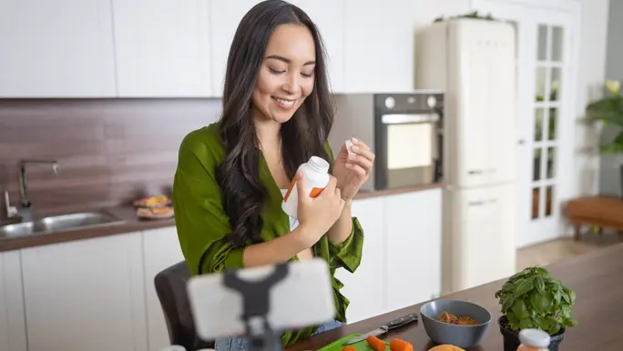 Smiling woman with long brown hair reading the label of her supplements and preparing a healthy lunch