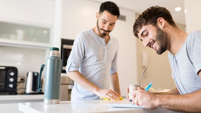 Two young dark-haired men are in the kitchen writing a list