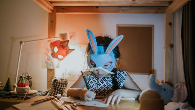 Young girl wearing a rabbit mask doing her homework