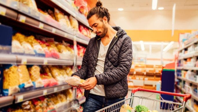 A young man is shopping in a supermarket and reading the label on a packet of food