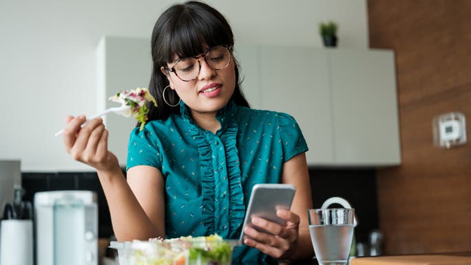 Young woman eating a salad and checking her phone