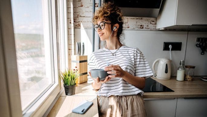 A woman stands in her kitchen looking out of the window