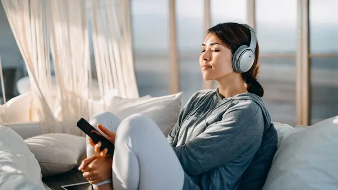 Woman in active wear relaxing on the couch listening to music through headphones