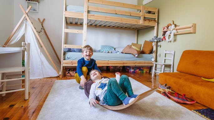 Two young boys are laughing and playing in a tidy and uncluttered child’s bedroom