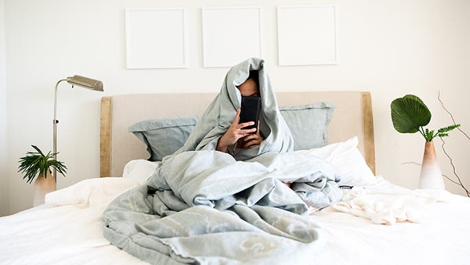 Cuddled in a pale blue quilt, a face peeks out while reading on the smartphone is you can actually catch up on sleep.
