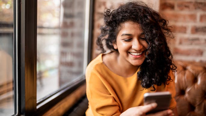 A lady laughs and smiles at her phone. It looks like she is using social media to keep connected with her friends. 