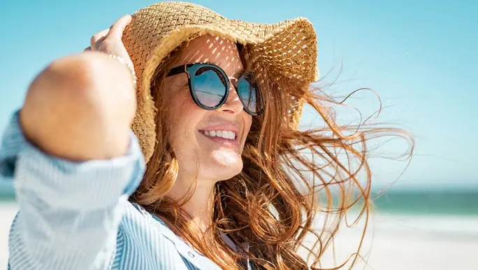 Red-haired woman at the beach in a striped shirt, sunglasses and straw hat