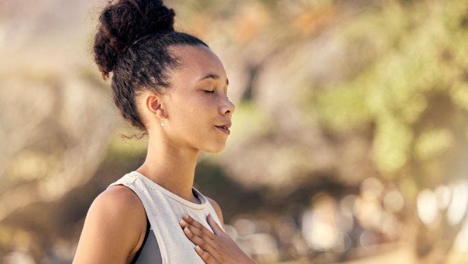 A young woman with her eyes closed and hands on her chest is practising breathwork