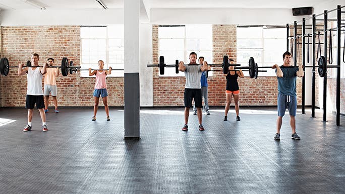 Seven people lifting barbell weights in a fitness class. Heavy lifting is the best way to build muscle.