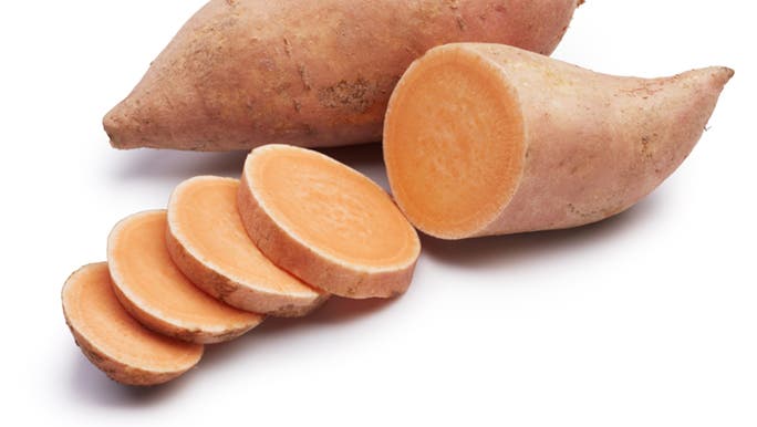 Raw sweet potatoes, one whole and one sliced are on a white background. 