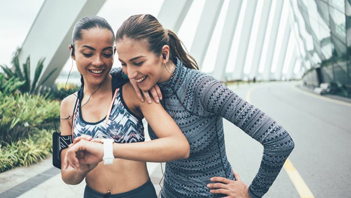 Two women in exercise clothes are looking at a fitness tracker on one woman’s wrist which is the smallest fitness tracker she could find.