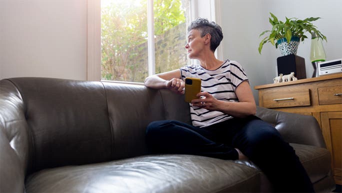 A middle aged woman is sitting on a sofa and looking wistfully out a window