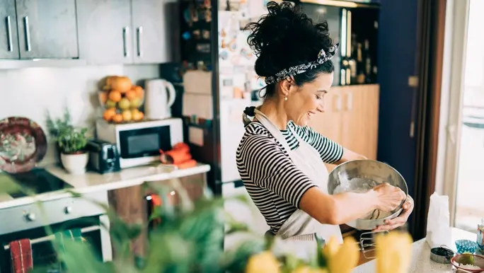 Happy woman in her kitchen wearing a black and white stripe top and apron making a calcium rich meal