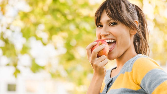 Smiling young woman eating a red apple in the park