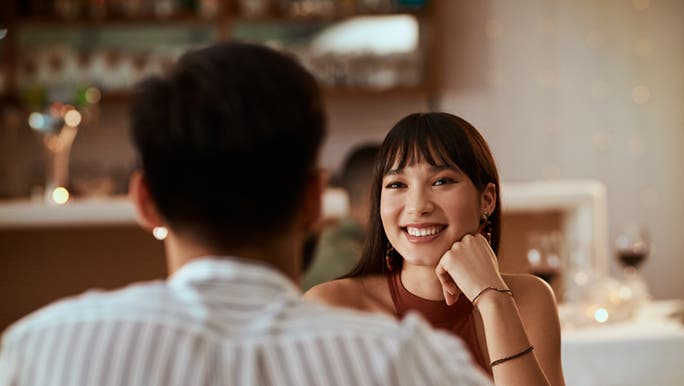 A couple are enjoying a meal in a fine dining restaurant, the woman is smiling at her date. 