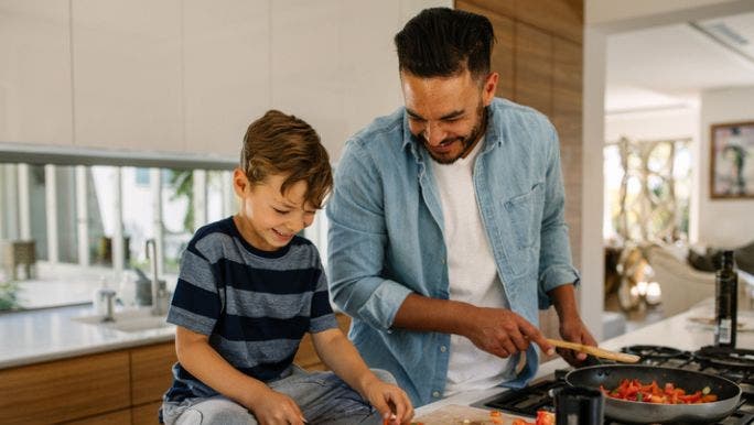 A young man and a young boy are standing at a kitchen bench cooking vegetables together