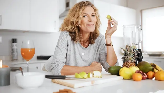 Woman in her kitchen leaning on the bench snacking on fruits and nuts