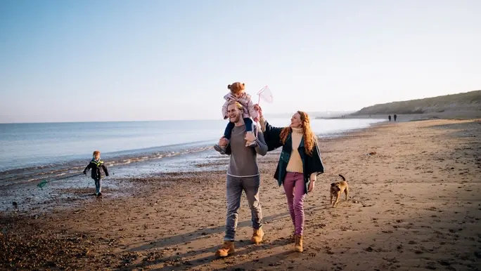 A family enjoying walking along the coast. It's cold outside so they are wrapped up warm.