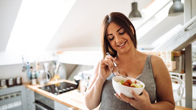 A smiling woman eats fruit out of a bowl in her kitchen as part of her gut reset.