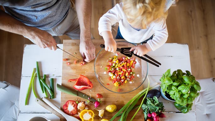 From above, a father and his toddler prepare a chopped salad. Cooking is a good way to introduce foods to picky toddlers