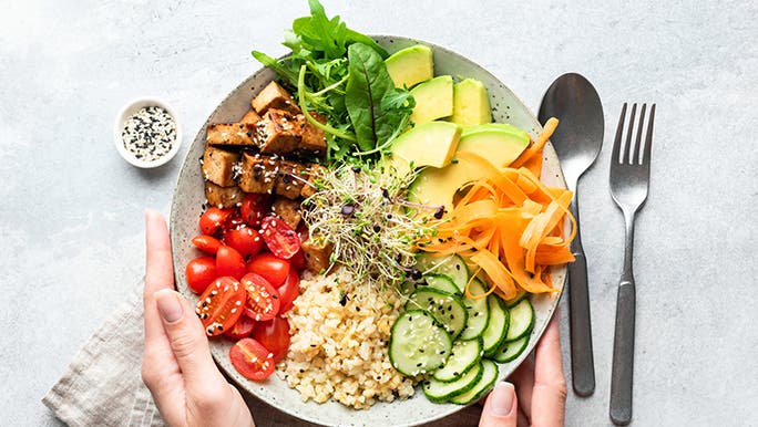 From above, two hands hold a plate that is piled with healthy food.