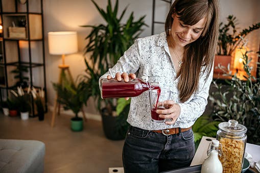 A young woman is smiling and pouring a glass of beetroot juice