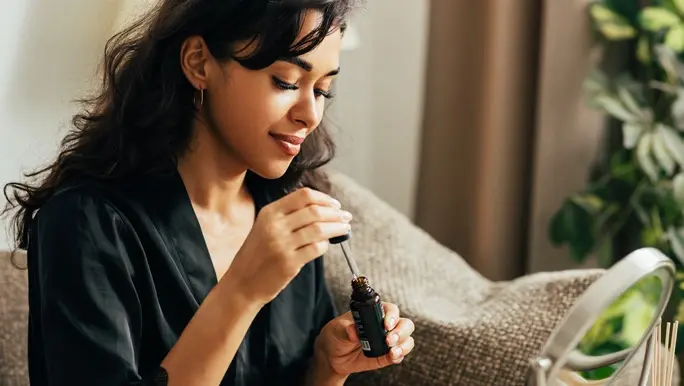 Young woman sitting on a couch holding a bottle of face serum preparing for applying