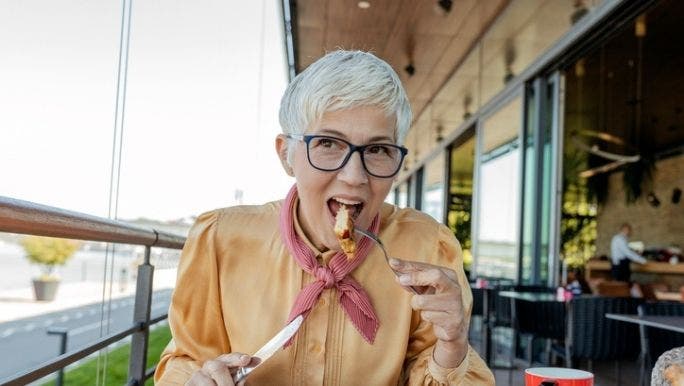 A senior woman is sitting at a cafe eating a small meal