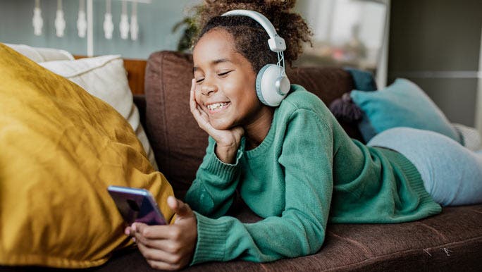 Smiling girl lying on the couch watching videos on a smartphone 