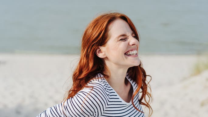 Woman with long red hair on the beach smiling with her eyes shut