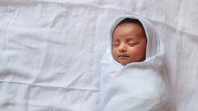Newborn baby asleep and wrapped in white muslin swaddling