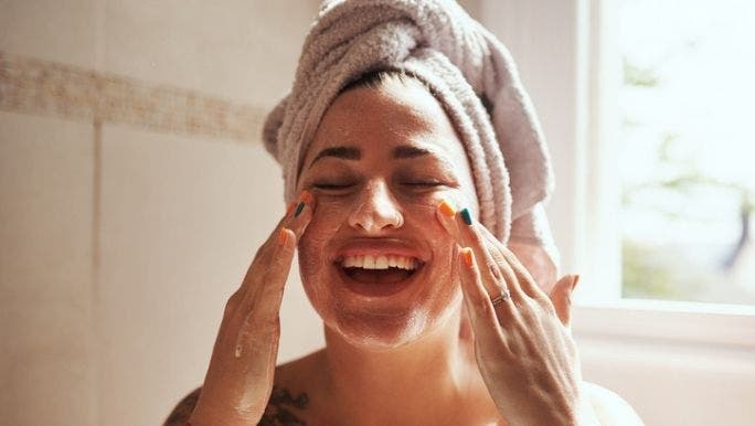 A woman with a towel wrapped around her hair is performing her daily skincare routine