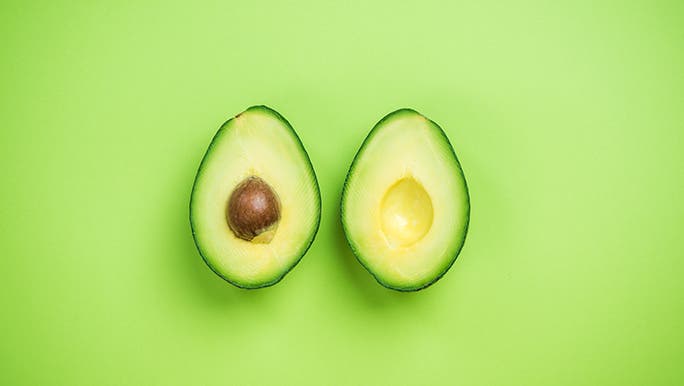 A halved avocado sits on a green background. 