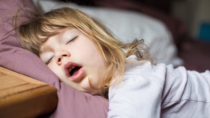 A close up of a sleeping toddler. Her mouth is open suggesting that she is snoring.