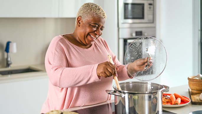 An older woman stirs food in a large pot on the stove as she cooks food that is building good gut bacteria.
