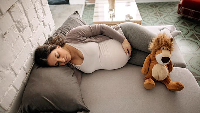 A pregnant woman lays on a large lounge - she is taking a nap. 