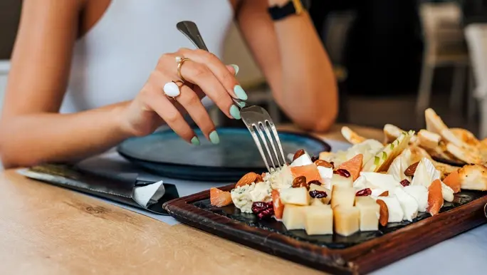 Woman wearing a white singlet picking cheese of a platter with a fork