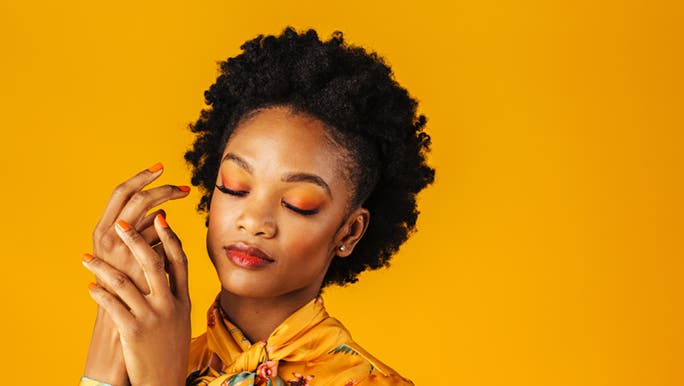 A lady is standing with her eyes closed, as she is holding both her hands together, embracing how soft her hands are and how they’re not dry or peeling.