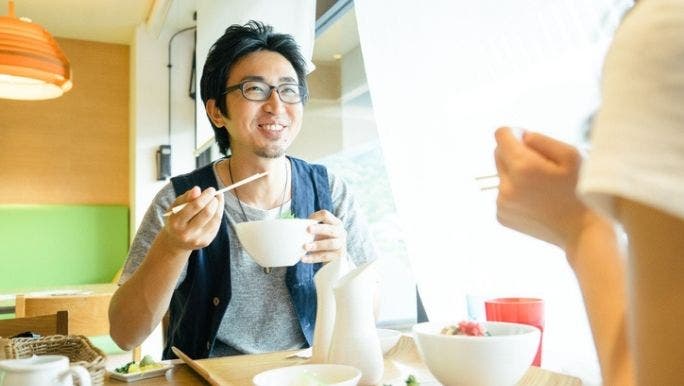 An Asian man is smiling as he eats a bowl of miso soup, which contains probiotics