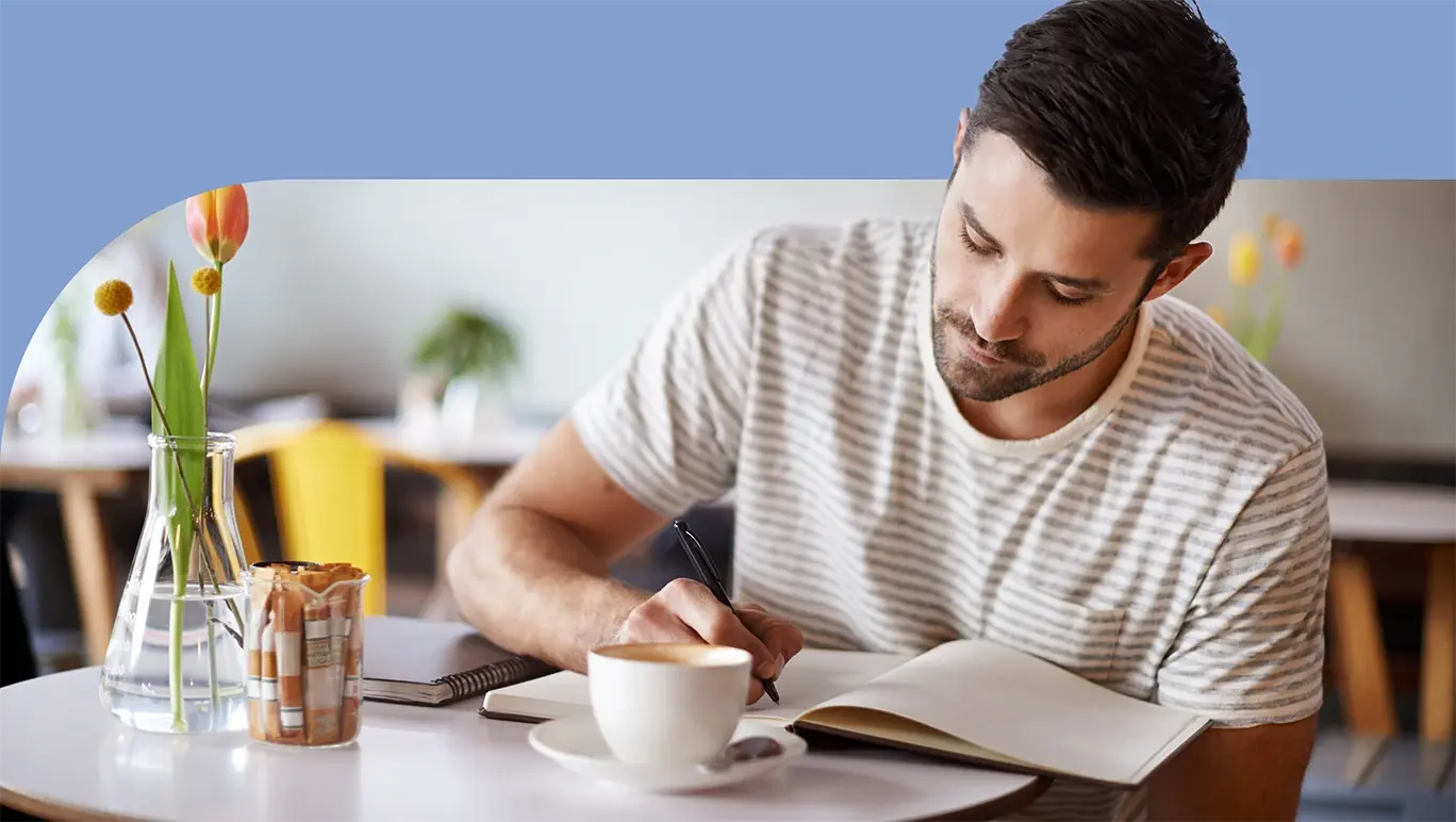 man writing in a diary while sitting in a cafe