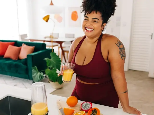 Happy young woman in red activewear drinking fresh vitamin C rich orange juice