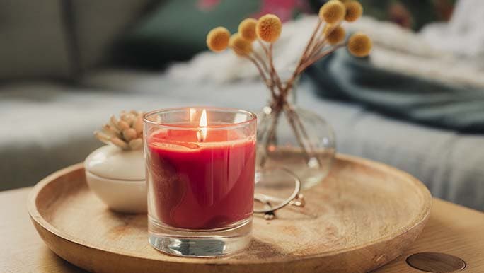 A beautiful red candle sits on a wooden tray and would make a perfect addition to a self-care gift box. 