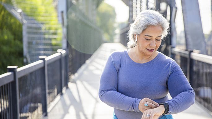 During a walk outside, a woman looks down to check her watch which is one of the best fitness smartwatches.