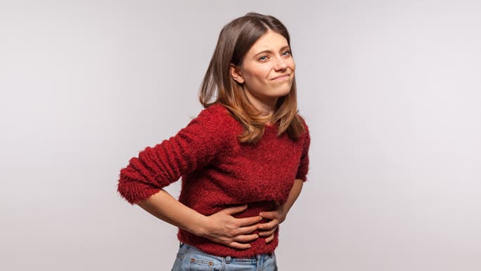 Lady in red is holding onto her belly, in pain. Feeling uncomfortable as she wonders why she is farting so much. 