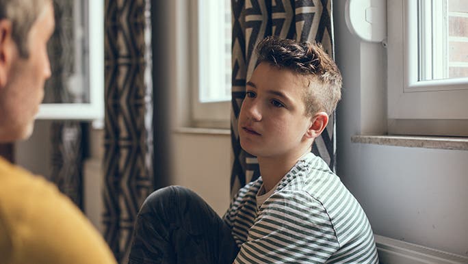 A father talks to his teenage son, the child looks sad. 