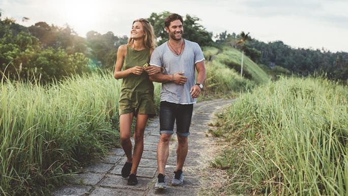 A couple happily walks along a path, they are enjoying the health benefits of walking. 