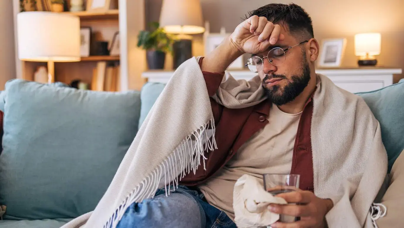 Man with the flu holding his head on the couch