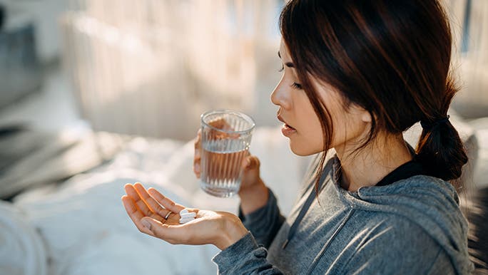 Woman with two pills in one hand and a glass of water in the other, she is trying to remember if she took her medication. 
