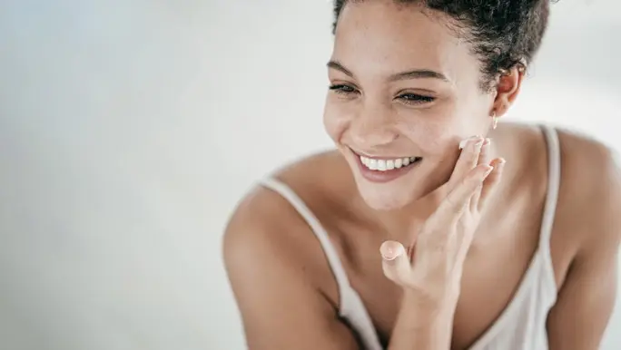 Happy smiling woman applying moisturiser to hydrate her skin
