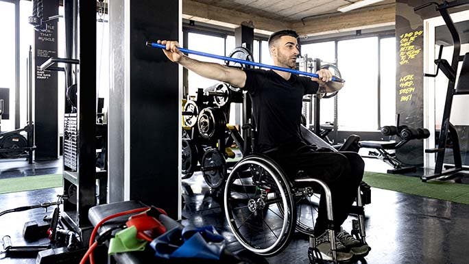 A man in a wheelchair is exercising at the gym thinking about how his friend asked him how to make himself go to the gym.